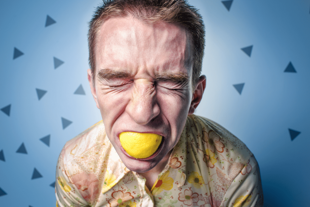 Mann beißt in eine saure Zitrone und verzieht dabei sein Gesicht.